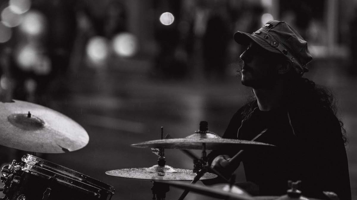 Joven baterista toca su instrumento bañado por la llovizna.