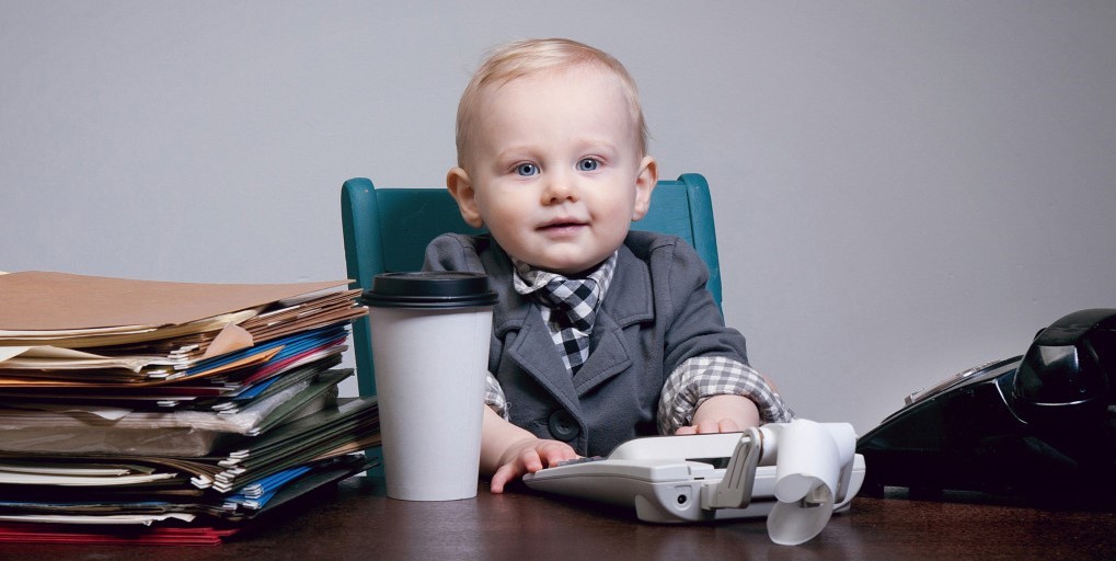 Picture of a baby in a buisness coat, sitting by a table