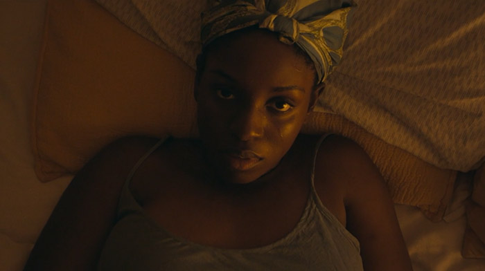 Further Away short film still of a black young woman lying in bed looking straight into the camera