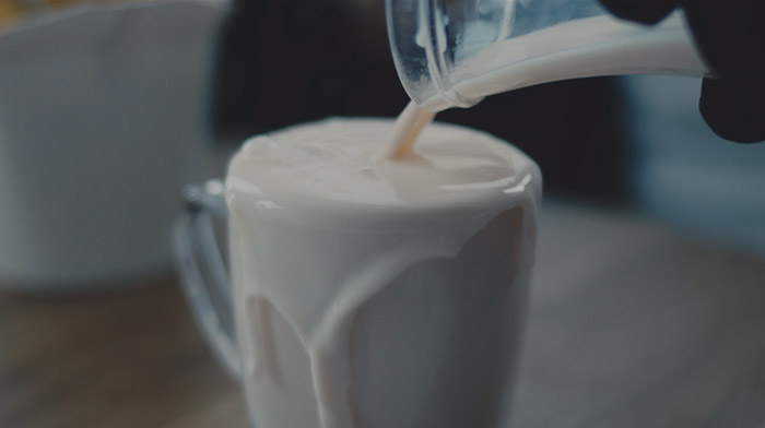 At Thirthy short film still of milk beaing poured into an overflowing glass