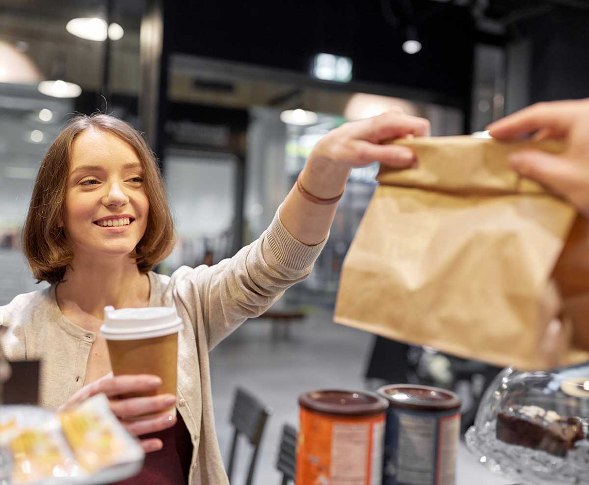 Female cafe customer holding coffee receiving takeaway order in paper bag