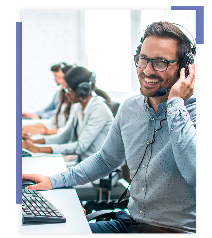 A imagem apresenta um homem de óculos sorrindo, utilizando um headphone e realizando atendimento (Call Center). Ao seu redor há mais pessoas fazendo a mesma atividade.