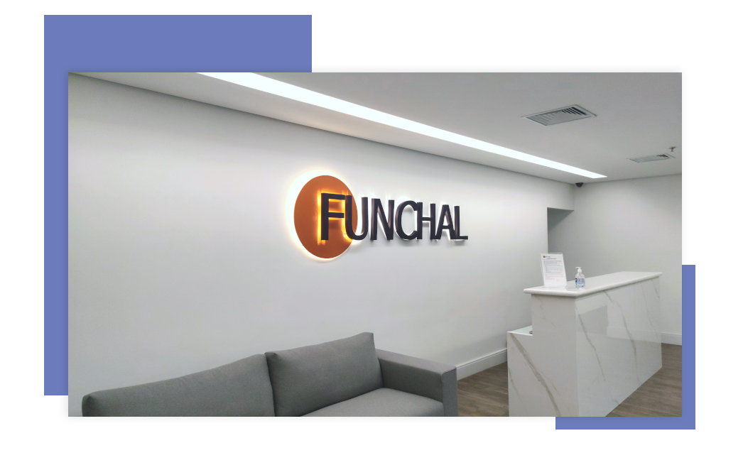 A imagem apresenta a recepção da Funchal Negócios com um sofá, uma mesa e o logo da empresa instalado na parede.
