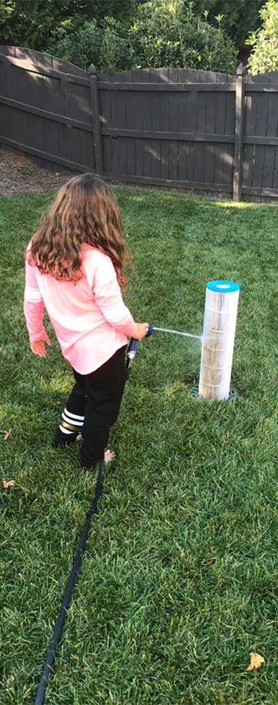 A child cleaning a pool cartridge filter by hand with a garden hose.