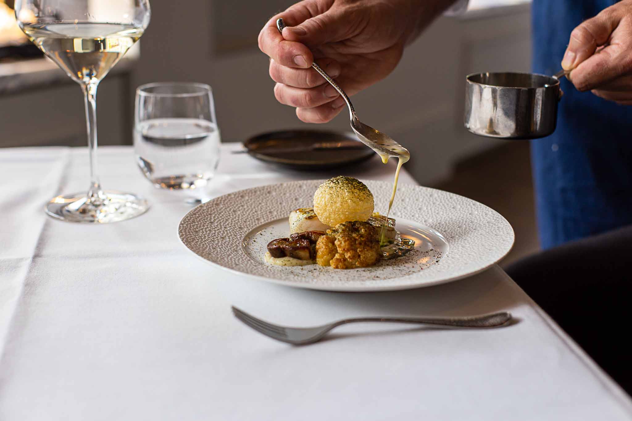 A chef pouring sauce over a dish in a french restaurant. Photo by restaurant photographer Louis Hansel.