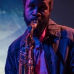 Headshot of Jerome Ellis playing an instrument with a blue background