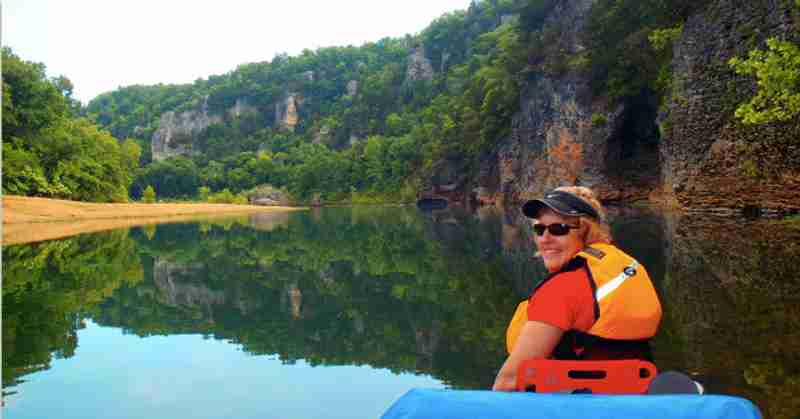 A kayaking on the Buffalo river surrounded by beautiful mountains.