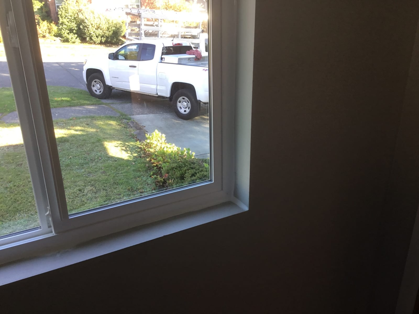 A clean window with a white frame allows the photo viewer to see a green lawn with shrubs and a white construction truck.