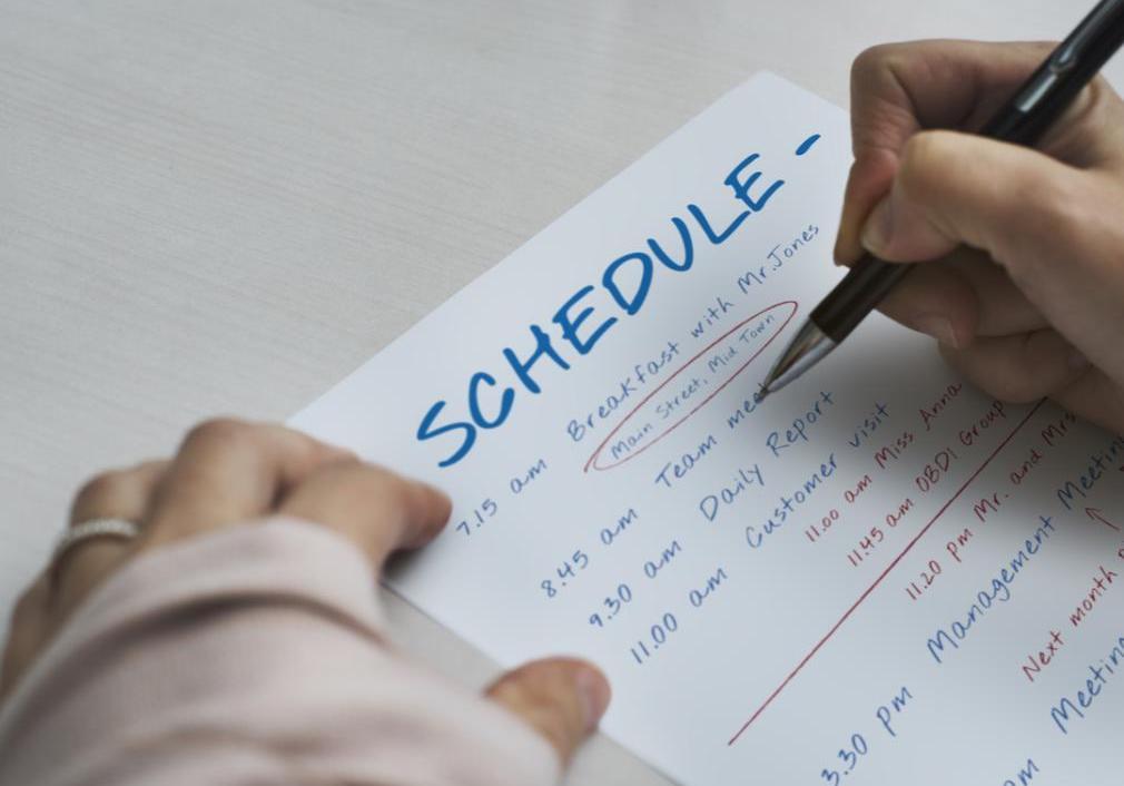 Someone is sitting at a desk jotting down their schedule for the day of what they'll be doing.