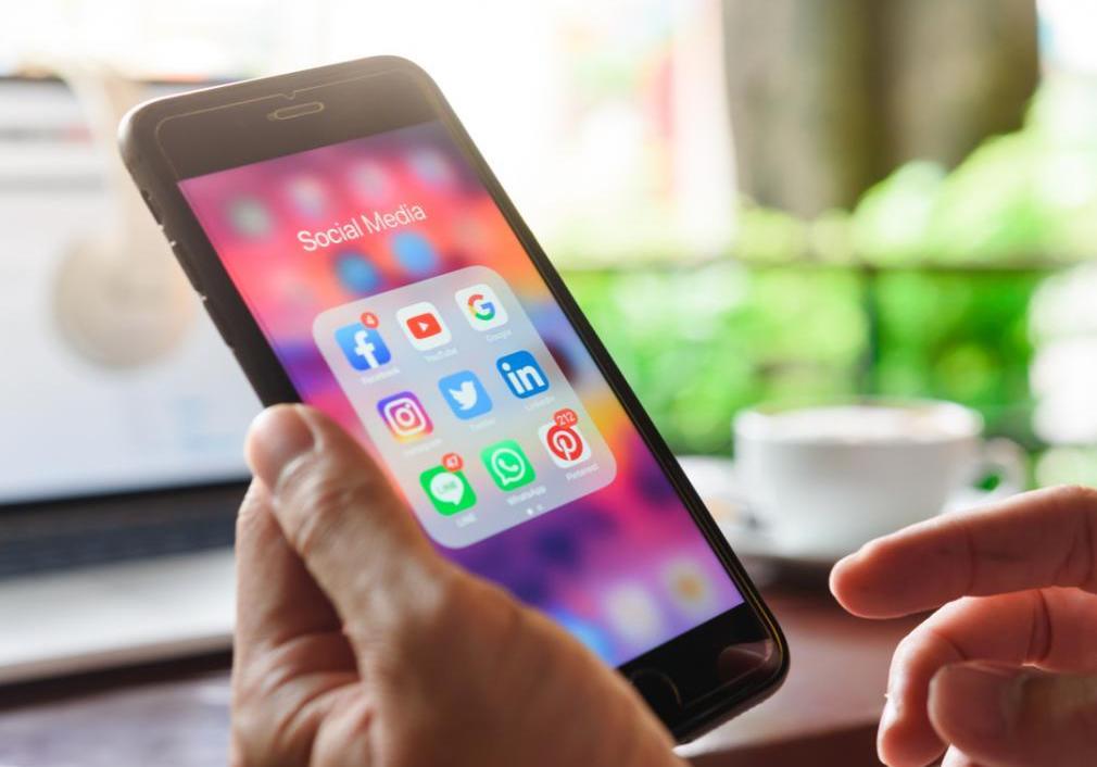 A man holds a cell phone that has social media app platforms displayed.