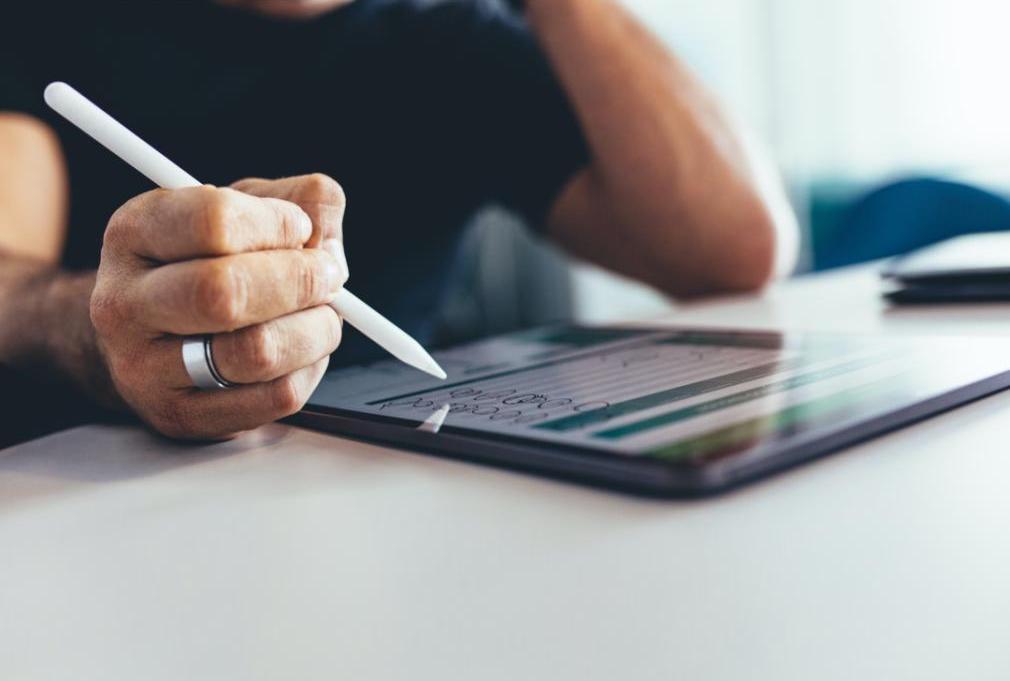 A man sits on his tablet at his desk going over projects that have to be completed.