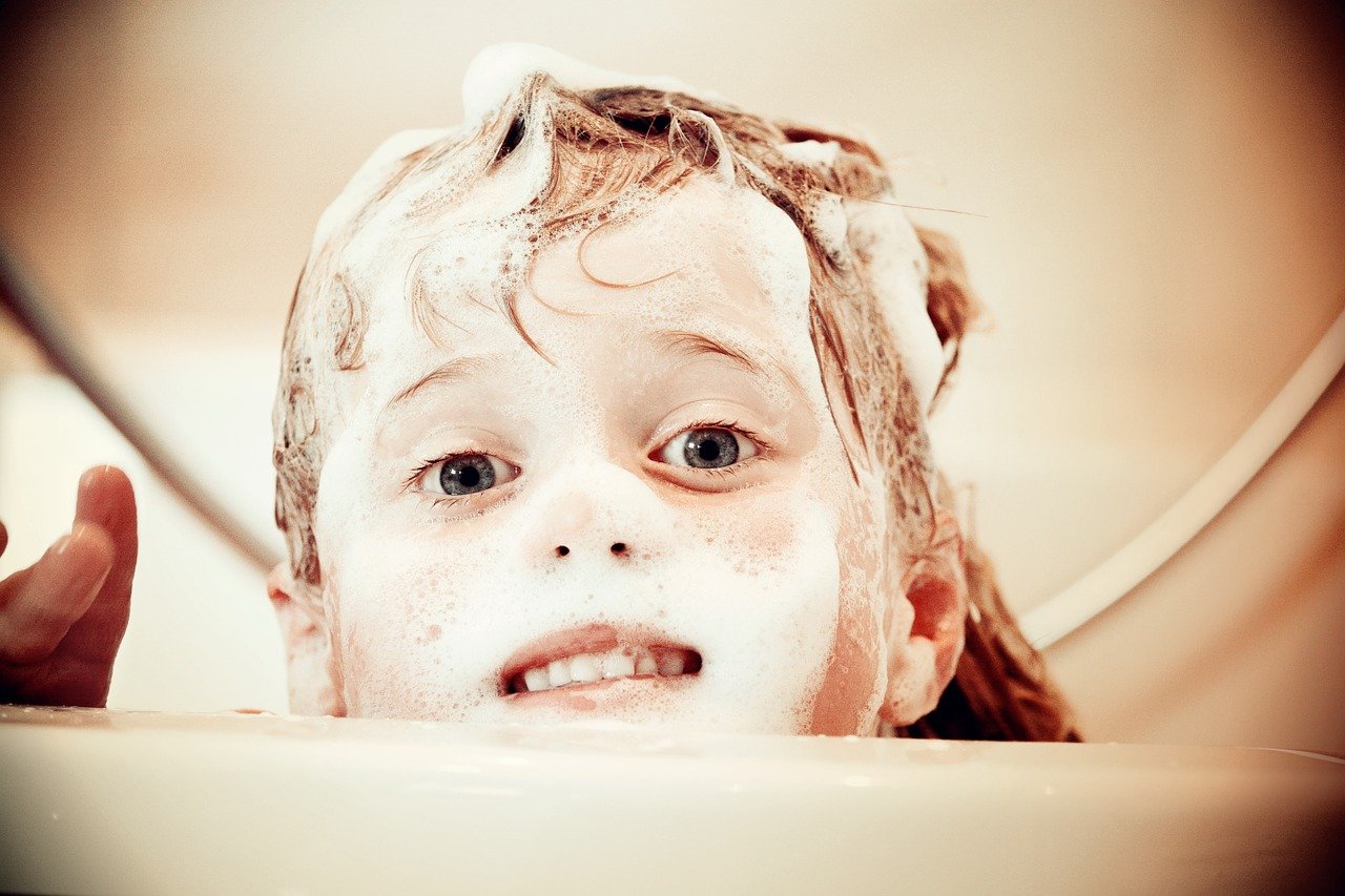 child with sudsy hair peeking out of tub