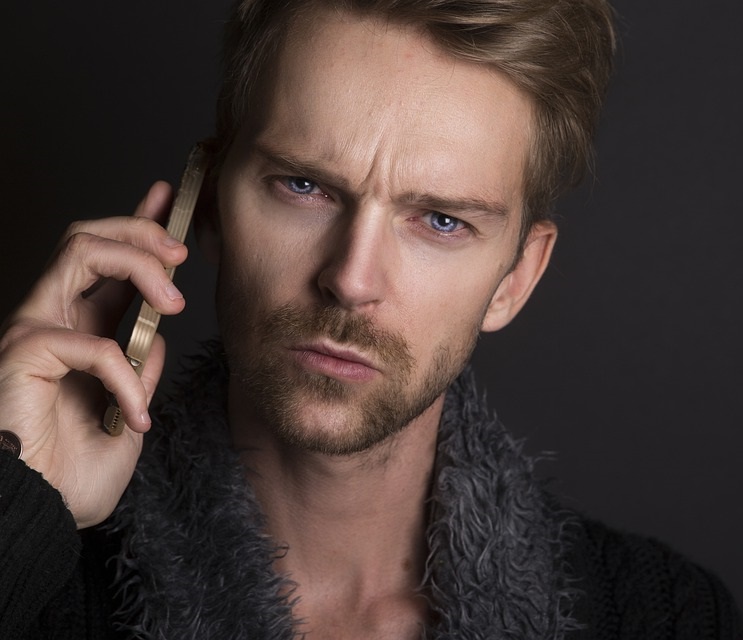 man with concerned look holding smart cellular phone up to his ear