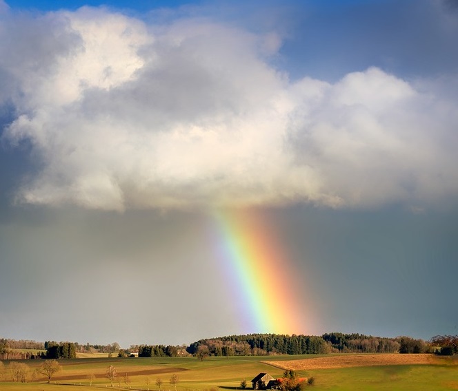 rainbow shining through clouds on to green pastoral farm