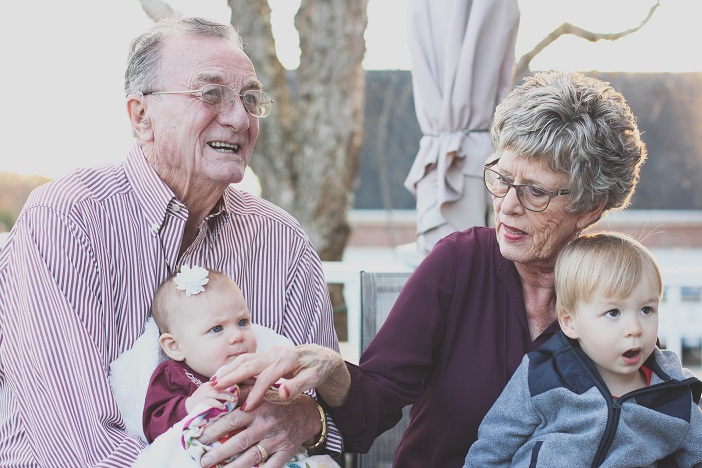 Grandparents, Elderly man and woman holding infant and toddler in their laps.