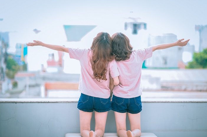 Rear view of two little girls looking out a large window, arms outstretched.