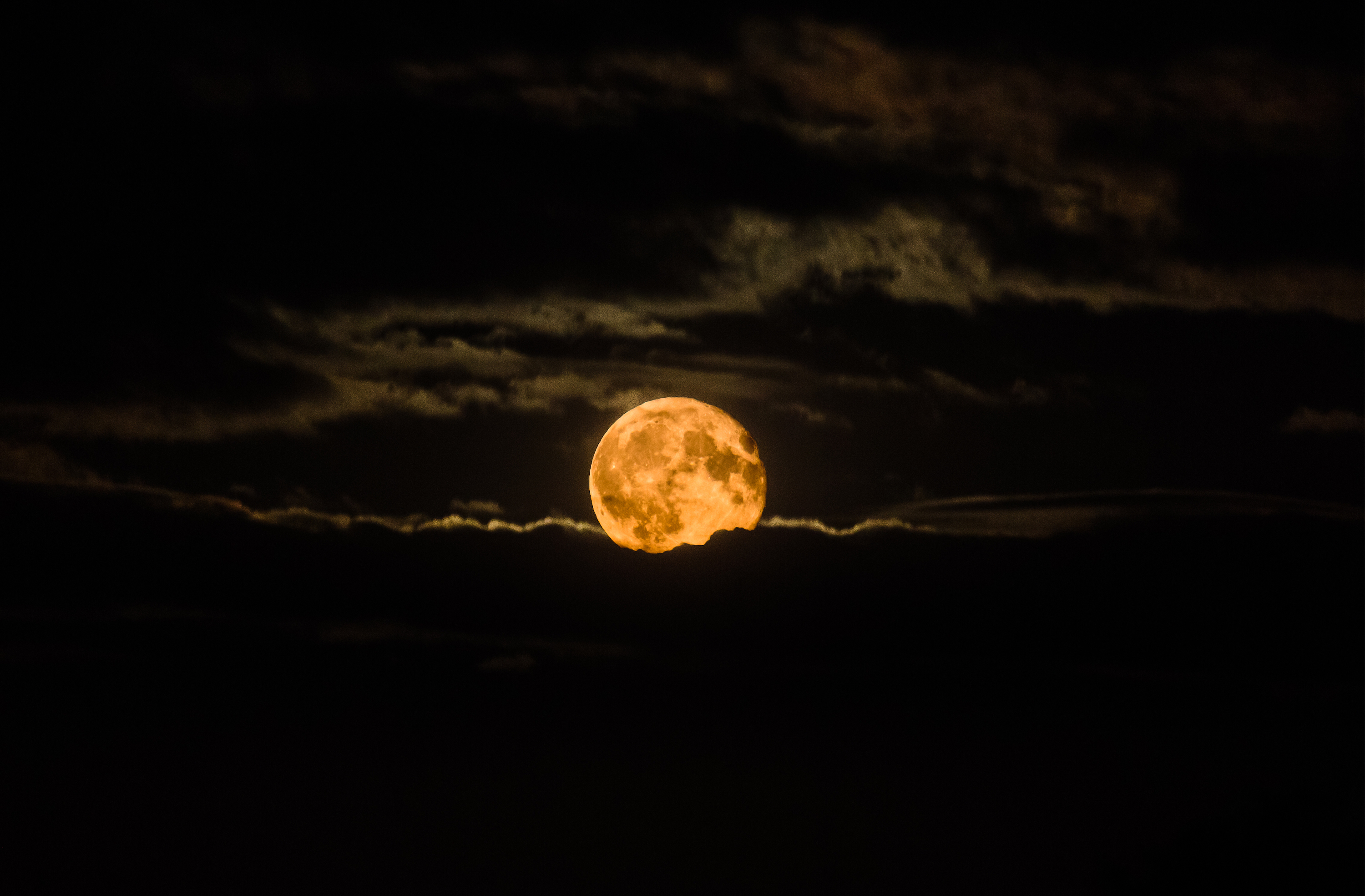 red 'Harvest Moon' rises through a drift of clouds on a September evening