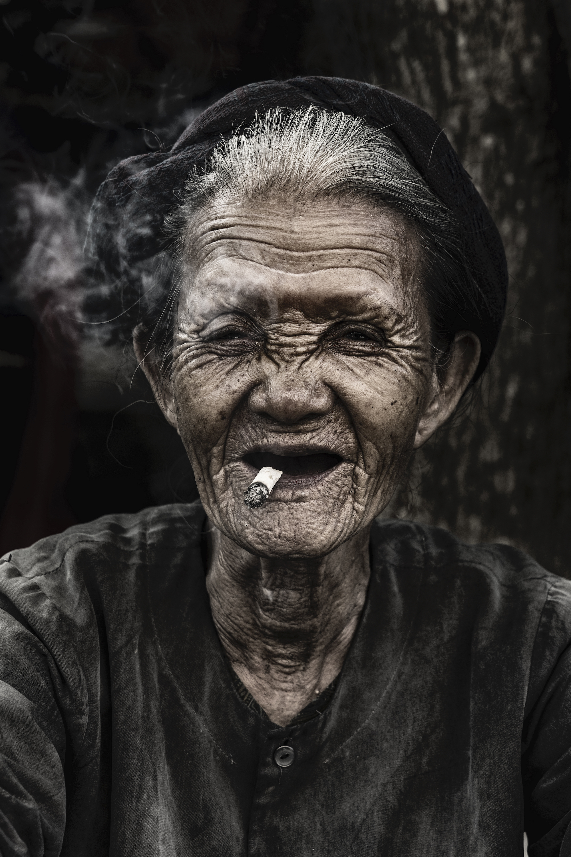 An old woman is smoking a traditional tobacco in a market at Hoian
