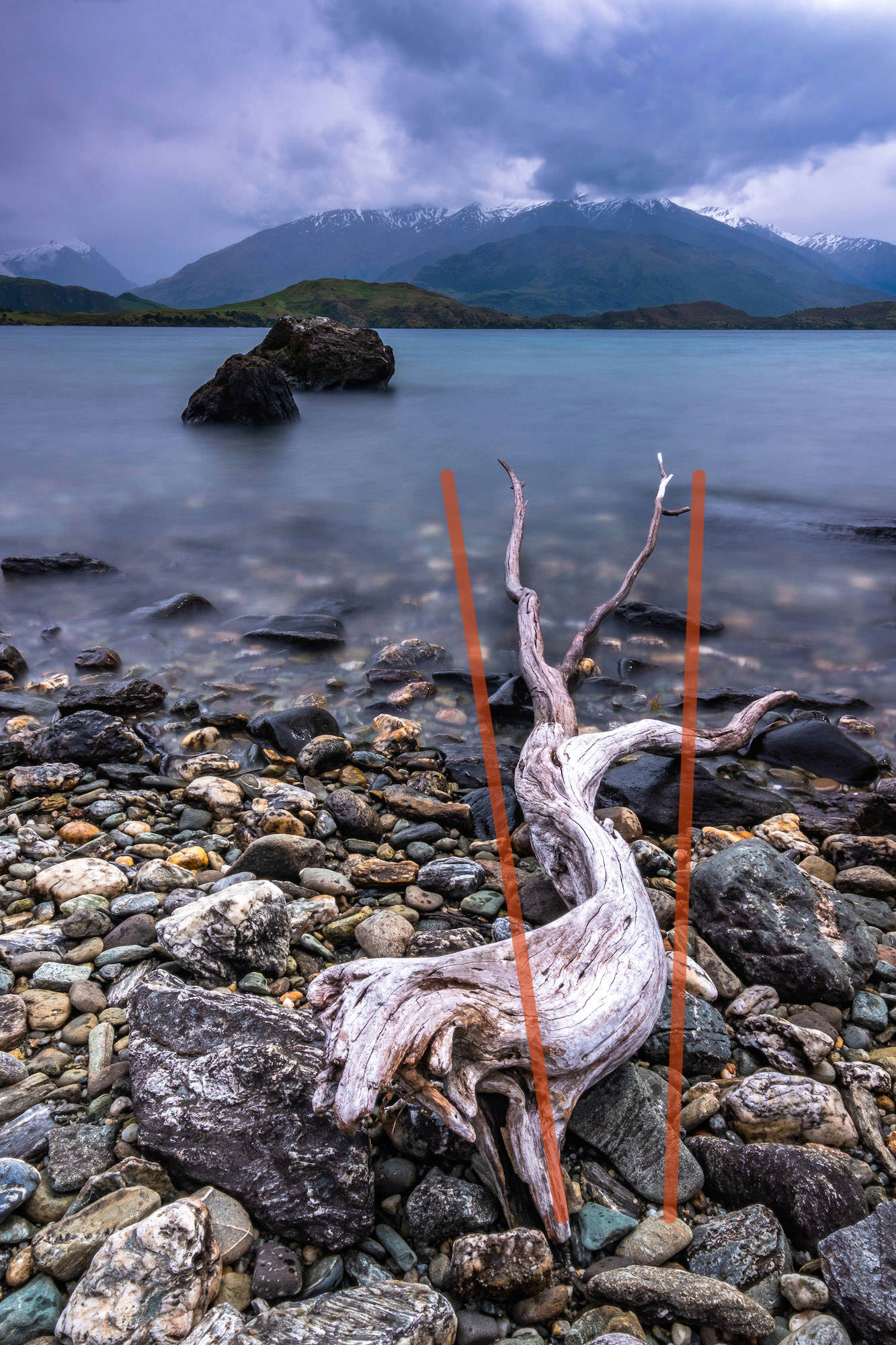 Washed up driftwood and pebbles make for a textured foreground as The Remakables are almost swallowed by low clouds; Queenstown, New Zealand. With added leading lines to show compositional technique.