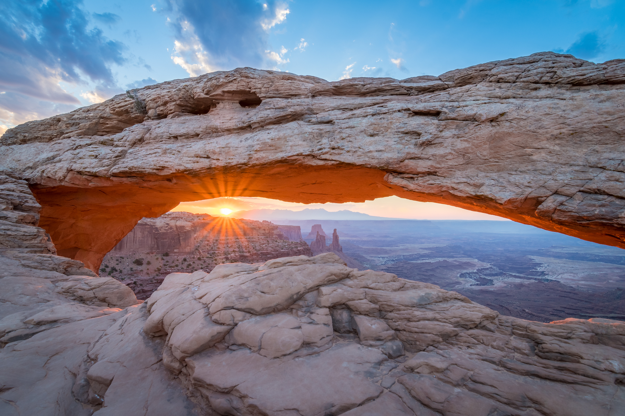 Sun rising in the distance under Mesa Arch, Utah, USA
