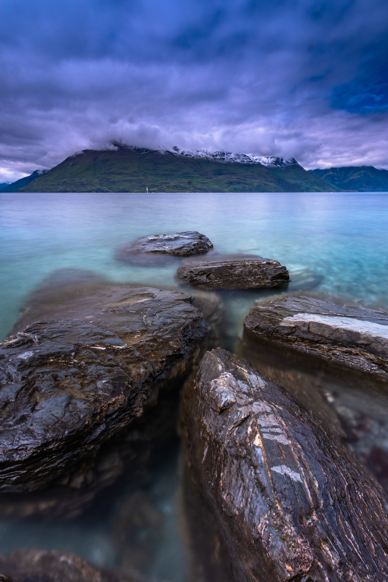 Vibrant blue water and storm clouds roll in over the Remarkables; Queenstown, New Zealand