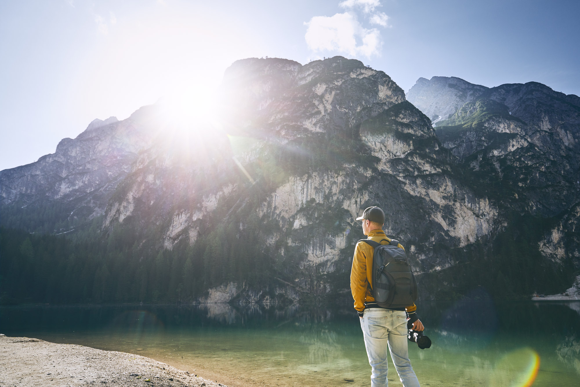 Young photographer holding camera against Lake Braies and mountains during sunrise. Dolomites, Italy