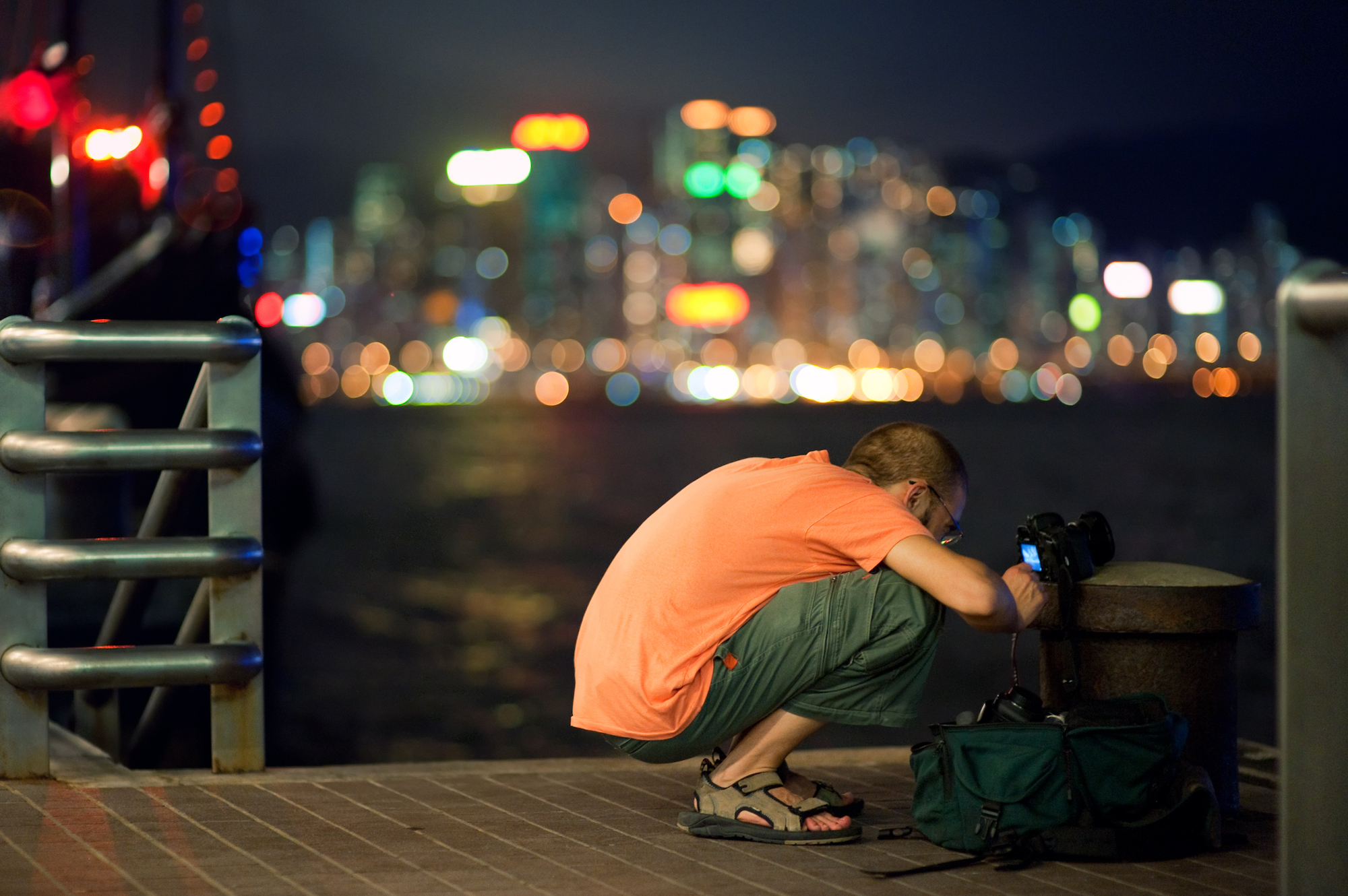 A photographer looks at the back of his camera against a night time cityscape