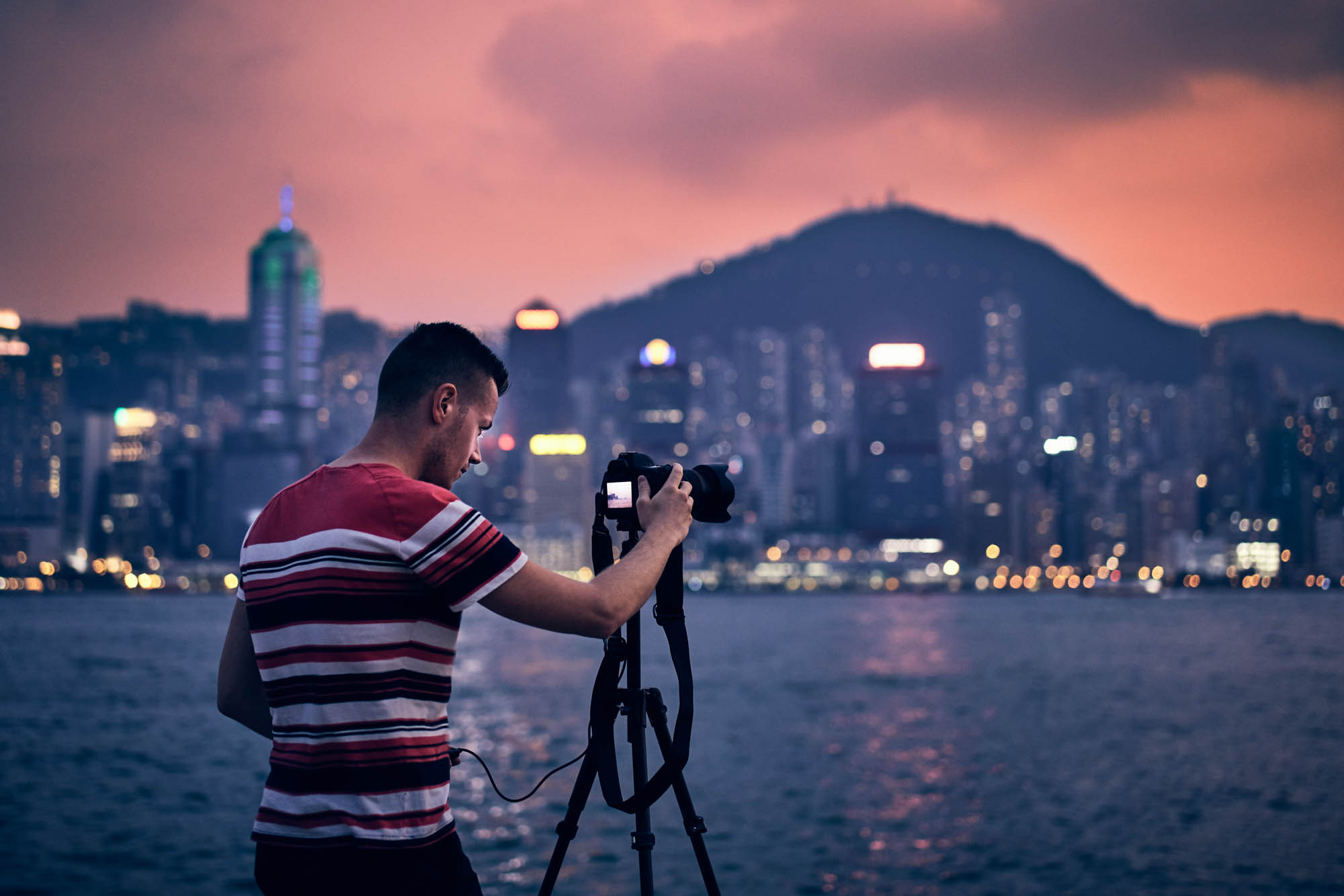 Young photographer (traveler) with tripod photographing urban skyline at sunset, Hong Kong.