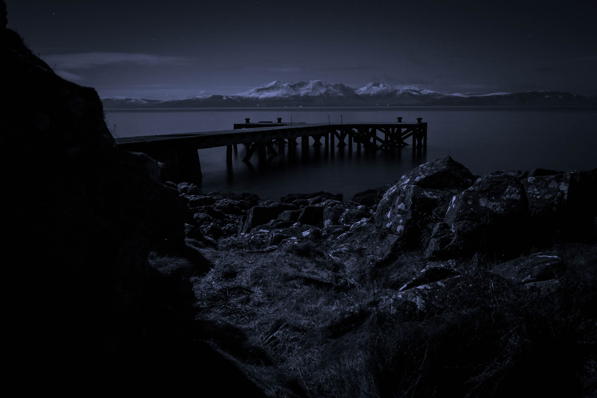 The Ayrshire hamlet of Portencross at night, looking out to the old pier, with the Isle of Arran in the distance. The sole light source is moonlight.