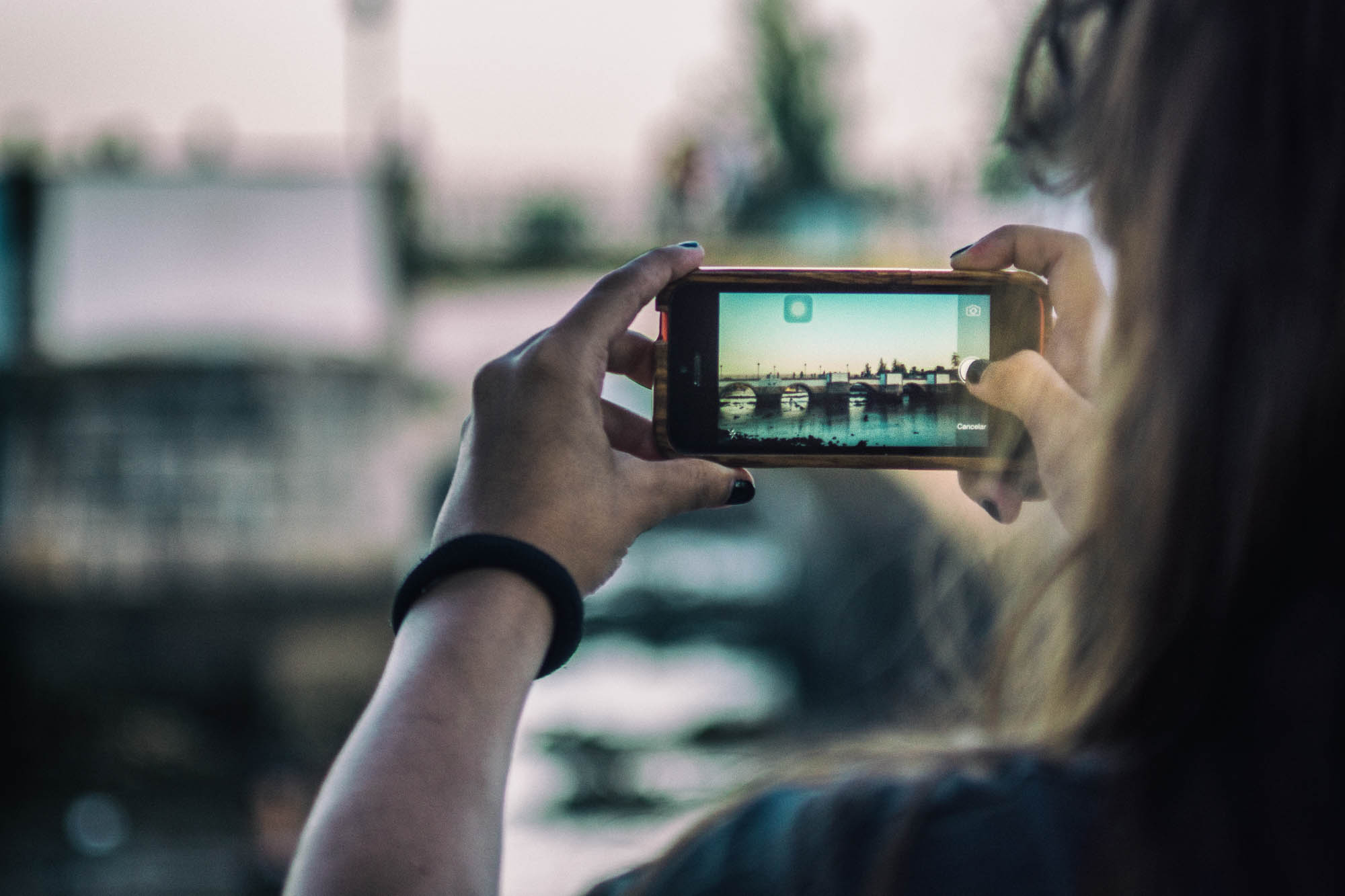 A girl using her iPhone to take a picture of an old roman bridge in Tavira, Portugal.