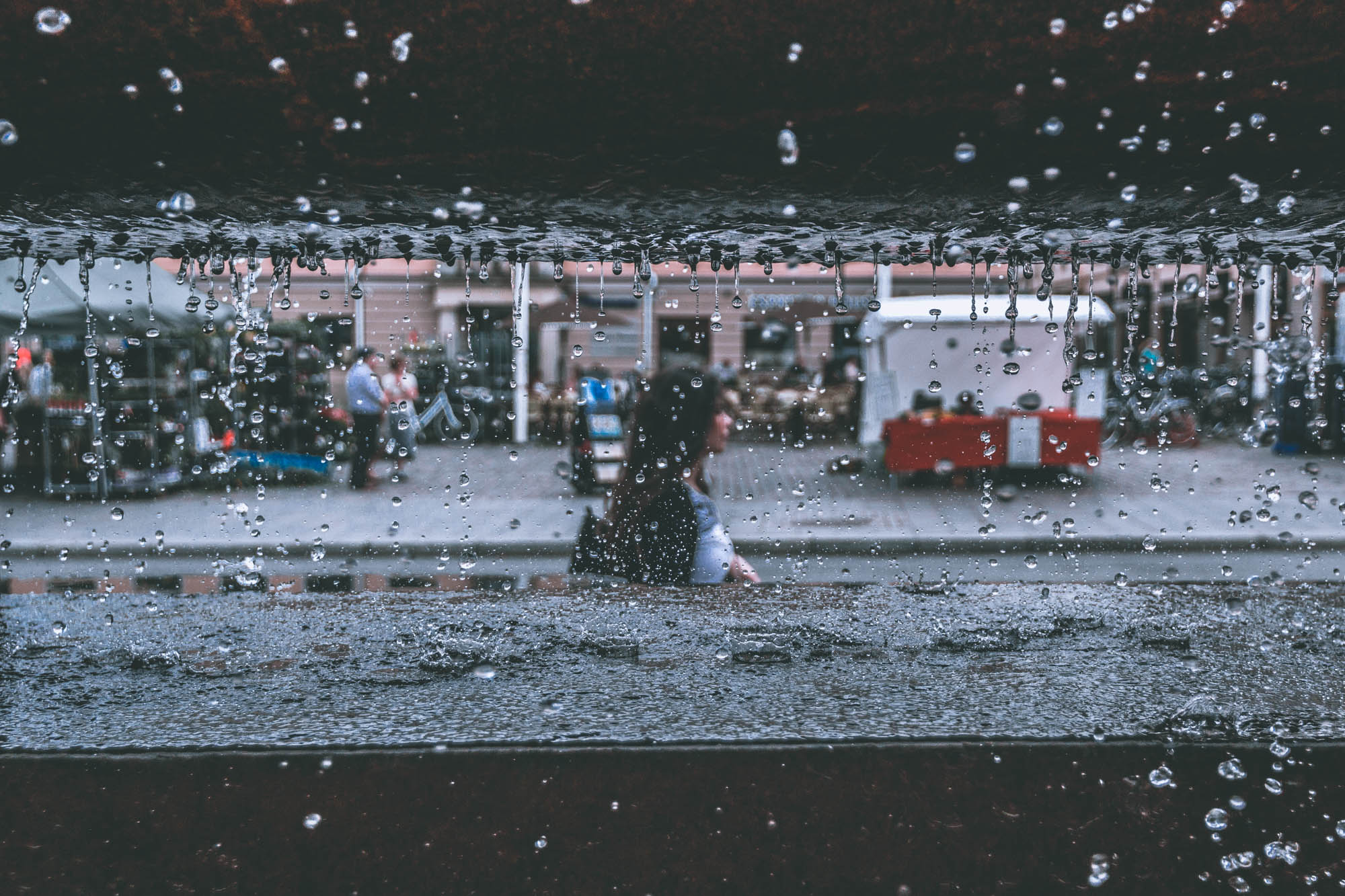 Girl walking on the street seen through fountain water drops. Scene from the street captured with manual focus.