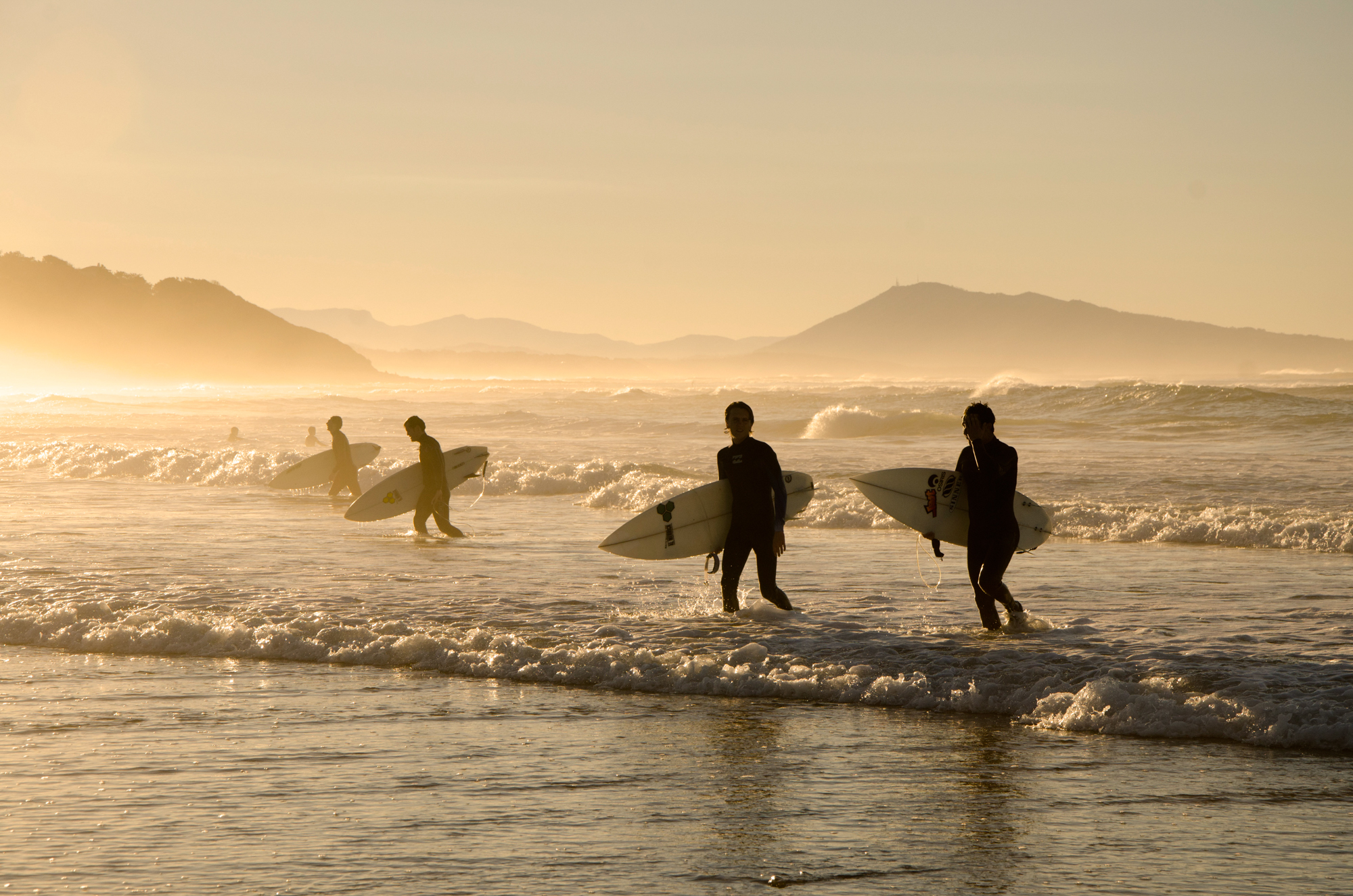Surfers leaving the waves behind at a beach near Biarritz during sunset, France.