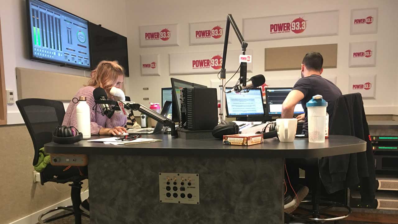 Radio hosts in the studio looking at 4 monitors and running their show.