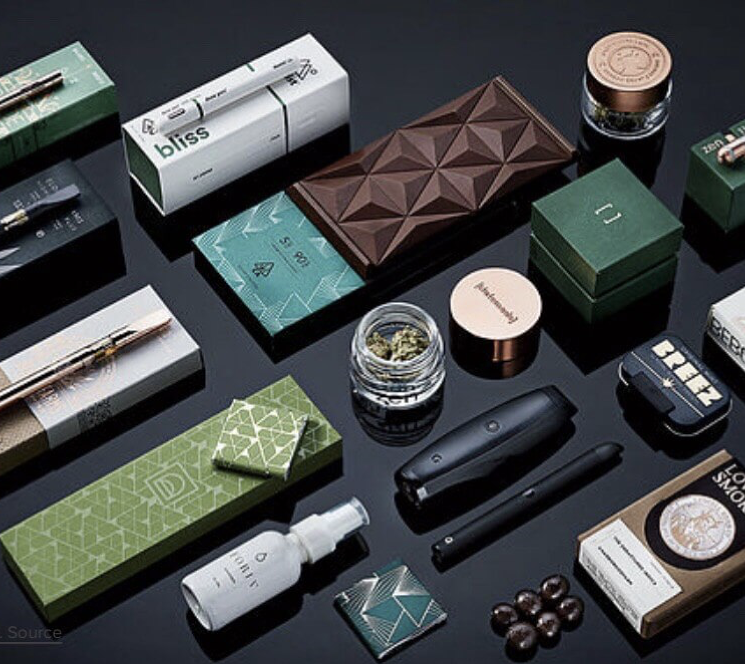 A collection of a cannabis products laid out diagonally on a black table.