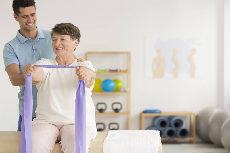 Physiotherapist helping older lady exercise in a private gym clinic