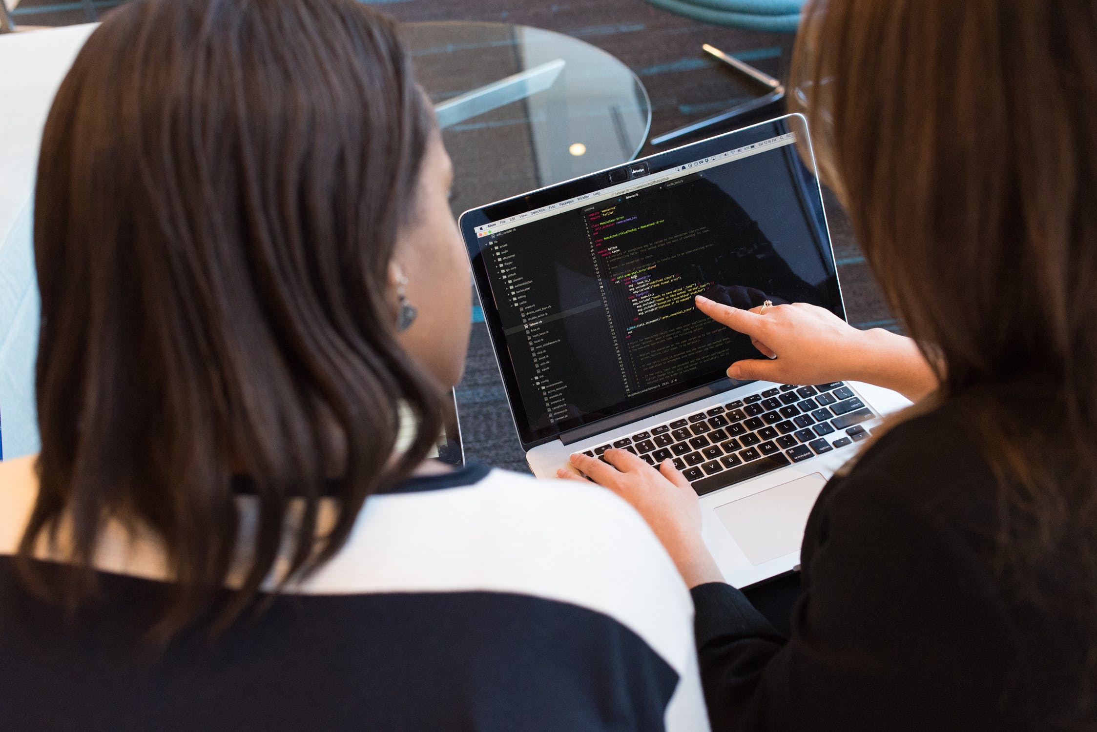 Two women looking at software code on a laptop.