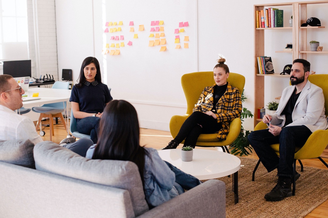 Group of coworkers seated on a sofa and yellow chairs facing each other.