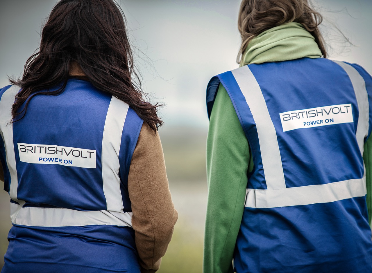 Two women facing away from camera wearing blue high vis vests with Britishvolt Power On branding.