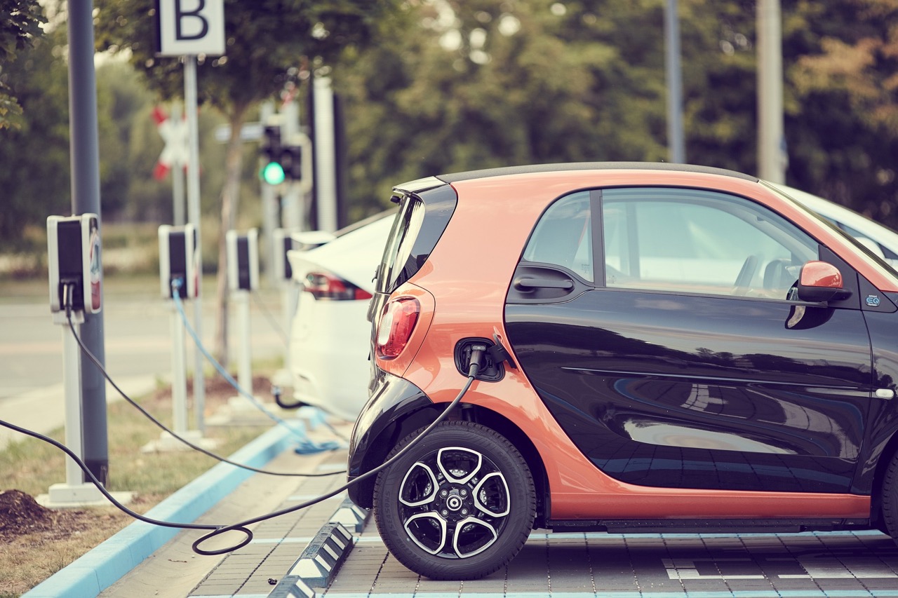 Small orange and black Smart car parked at an electric charging station.