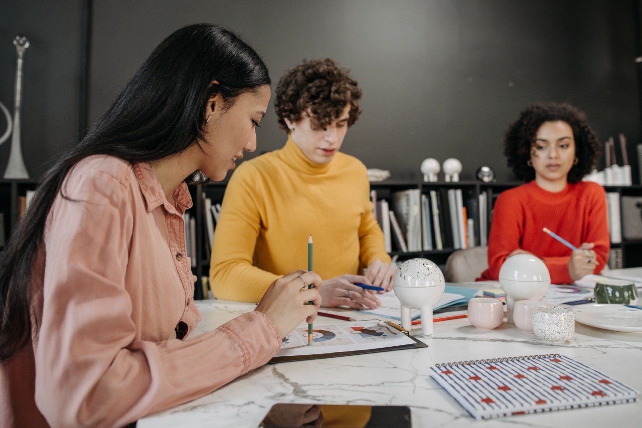 Three people seated around a white marble table looking at graph documents.