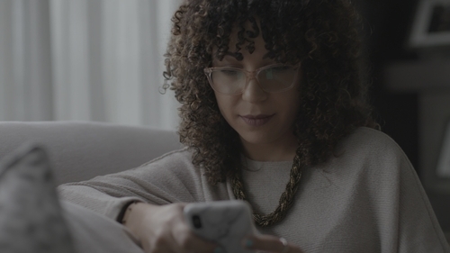 Woman on couch looks down at cell phone in her hand.