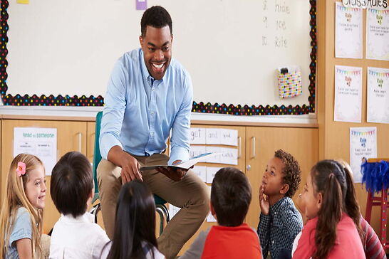 A teacher happily teaching young students sitting on the ground.
