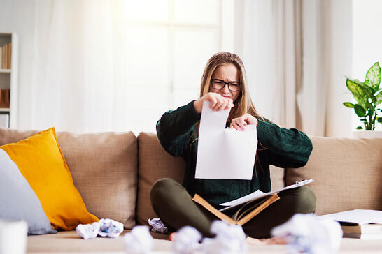 A girl sitting on a couch ripping up a piece of paper.