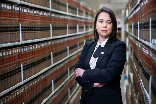 A woman standing with her arms crossed in a law library.