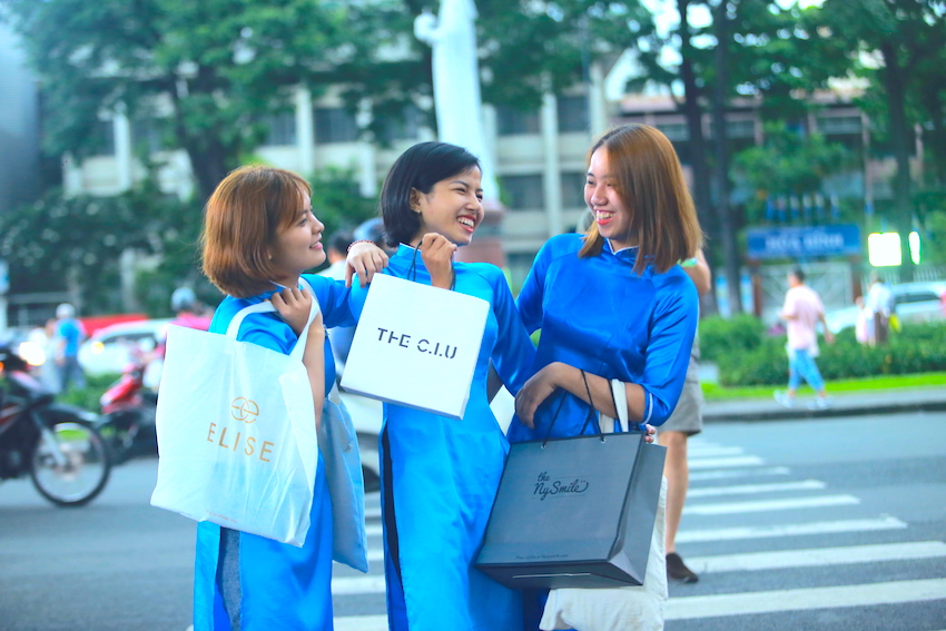 nữ hướng dẫn viên trong trang phục áo dài cầm túi lưu niệm