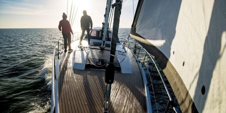two sailors standing on a sailboat whilst under way