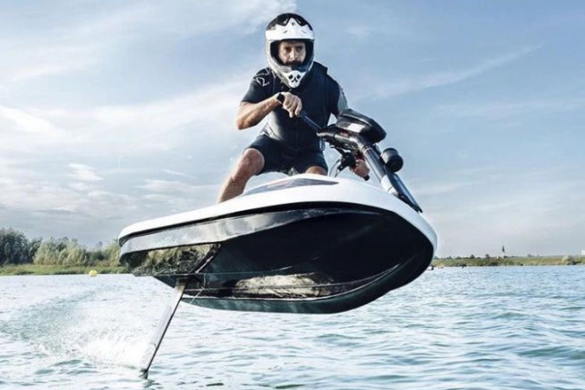 A man with a helmet riding a foiling scooter in the water whilst standing up