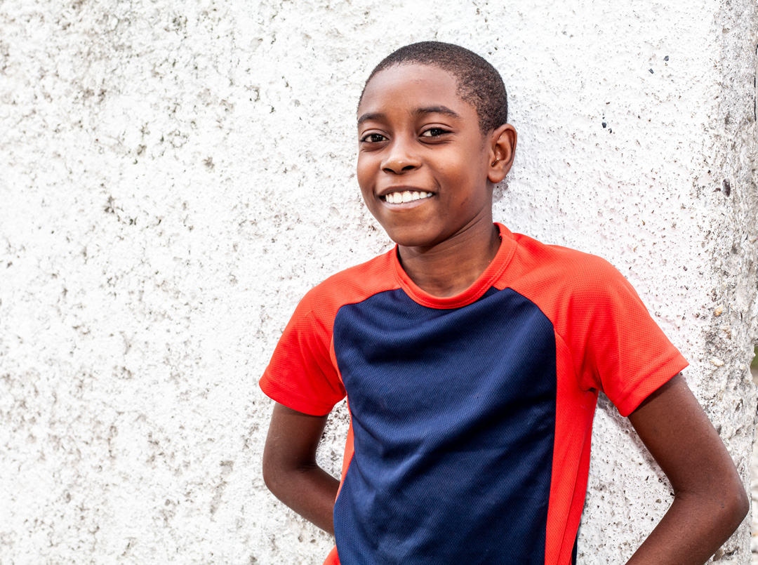A boy smiling while leaning on a wall.