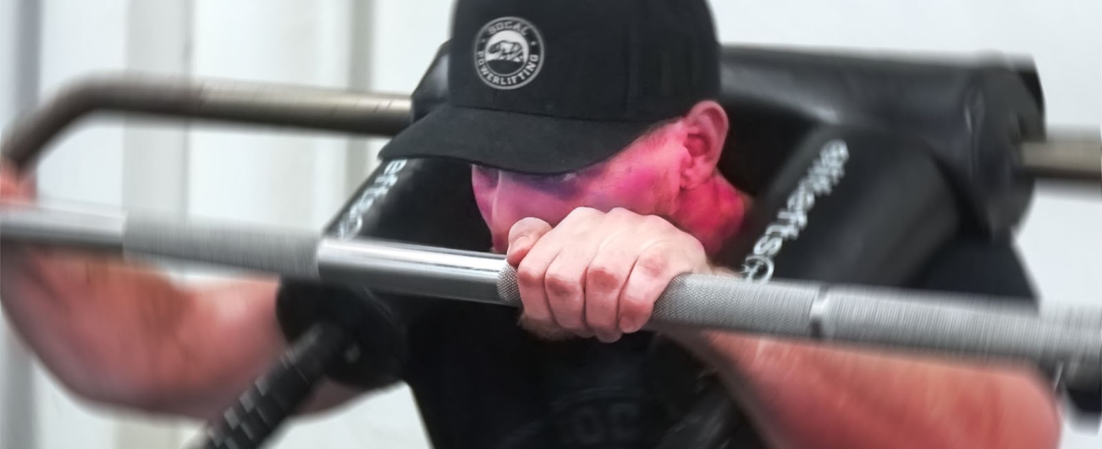 close up to man's face while squatting. his face is comically red from exertion.