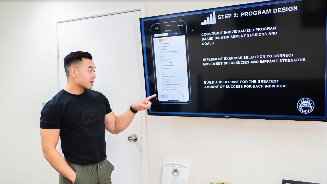 SoCal Powerlifting coach pointing to image of phone with workout program on its screen.